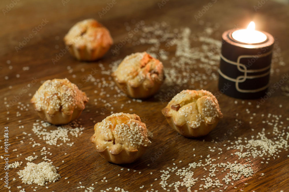 Five salty muffins with sausage, cheese and sesame near candle on wood table.