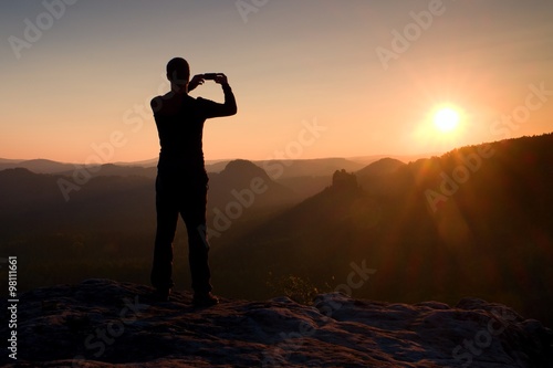 Hiker is taking photo by smart phone on the peak of mountain at sunrise.