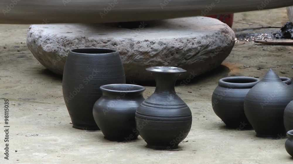 Freshly produced black clay pottery located on the ground with the traditional potter wheel spinning at the background in Tangail, Bangladesh. Freshly produced black clay pottery located on the ground with the traditional potter wheel spinning at the background in Tangail, Bangladesh.