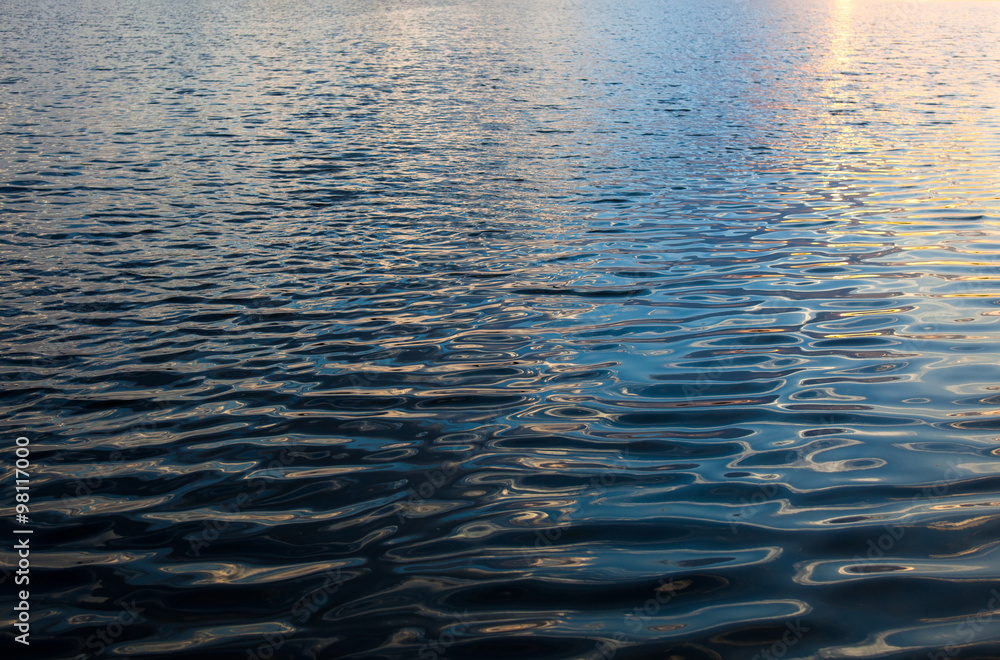 Water surface with ripples and sunrays reflections