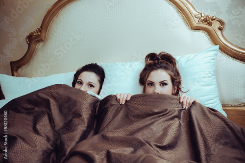 Fototapet Portrait of sexy beautiful young ladies in bed and looking at camera
