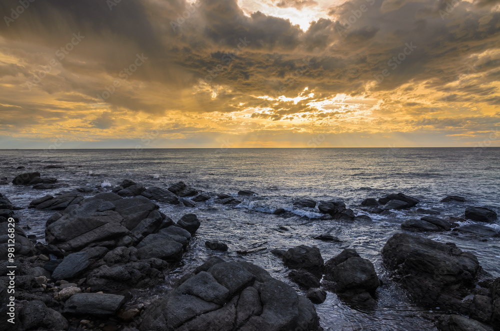 Dramatic sunset at the ocean with boulder rocks