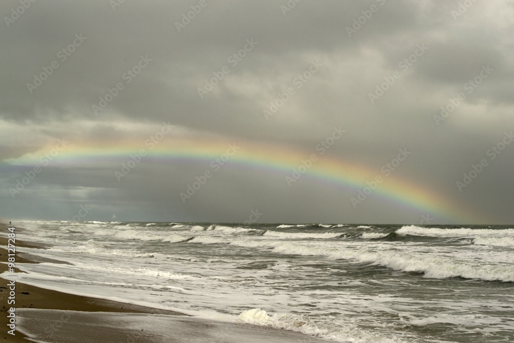 Tropical beach with waves breaking and rainbow in stormy dark sky