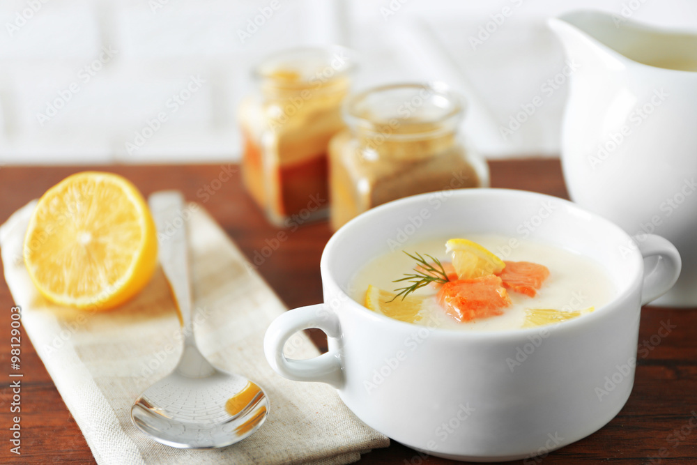 Delicious salmon cream soup on wooden table, which served with sliced lemon and spices Delicious salmon cream soup on wooden table, which served with sliced lemon and spices