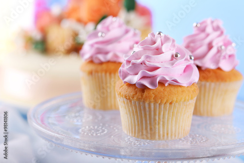 Tasty cupcakes on stand and cake, on table, on color background