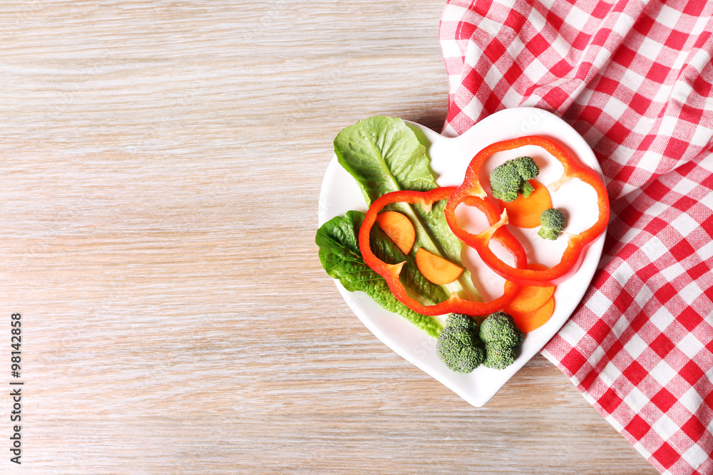 Useful cut vegetables on a plate in the form of heart on wooden table top view Useful cut vegetables on a plate in the form of heart on wooden table top view