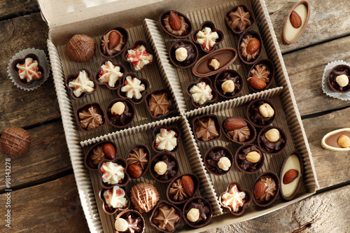 Different chocolate candies in paper box on wooden background, close up