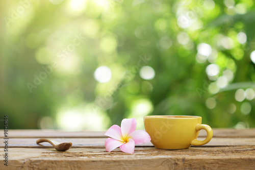 yellow coffee cup with flower and wooden spoon on wooden table