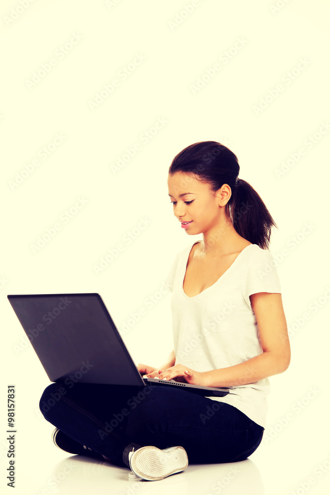 Naklejka premium Teen sitting cross legged with laptop.