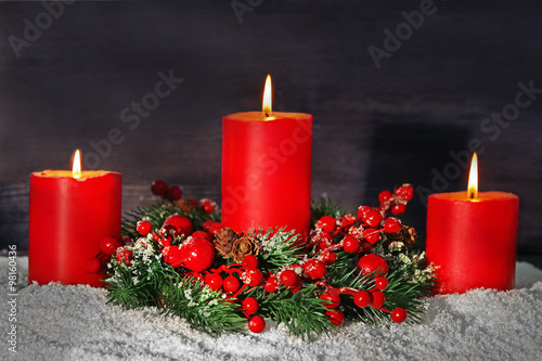 Burning candles and rowan with snow on wooden background