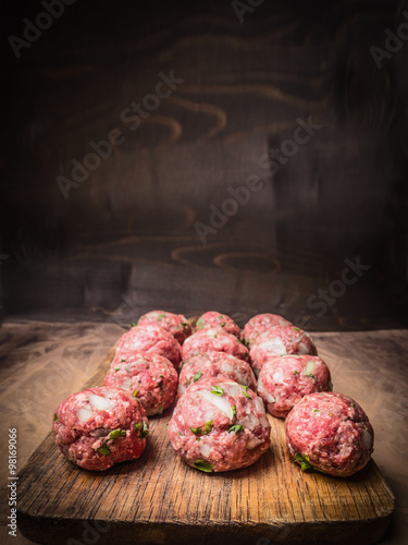 raw minced meat balls with herbs and onions on a vintage cutting board close up