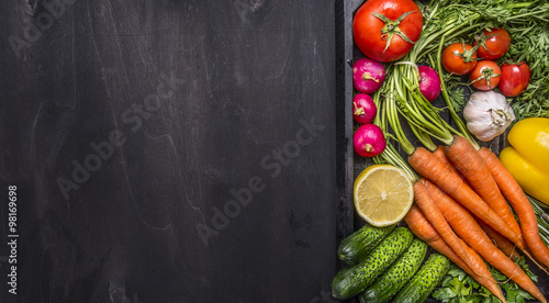 Delicious assortment of farm fresh vegetables with fresh carrots with cherry tomatoes, garlic, lemon radish, peppers, cucumbers on wooden rustic background top view border, place for text