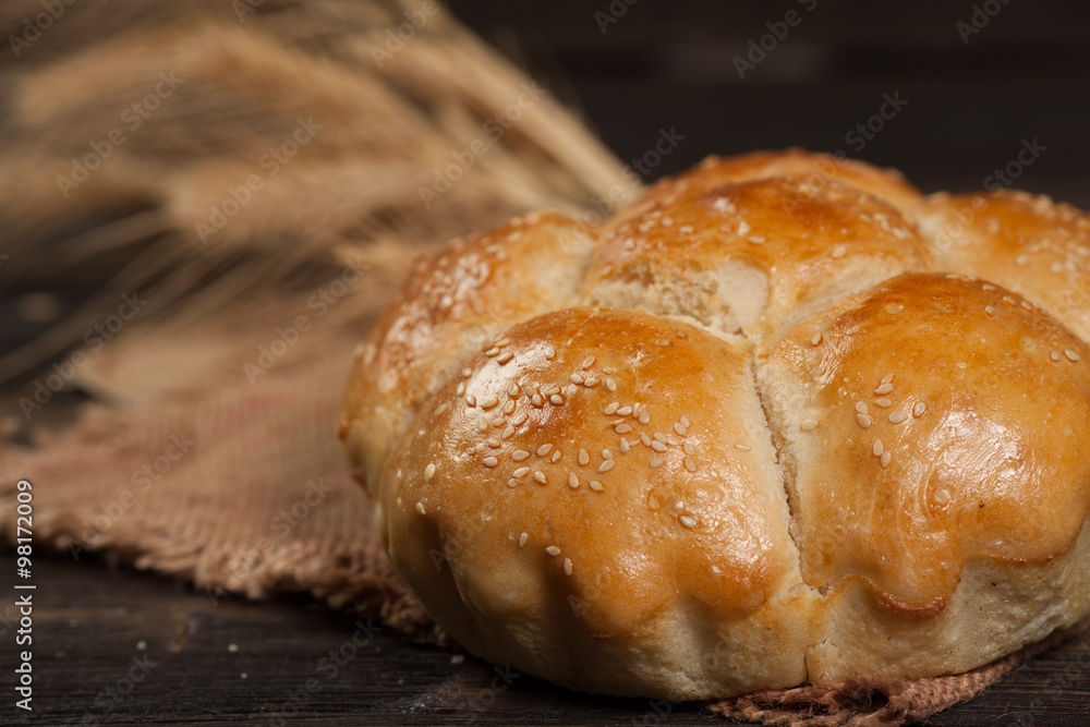 freshly baked bread with sesame seeds, wheat ears, vintage wooden background