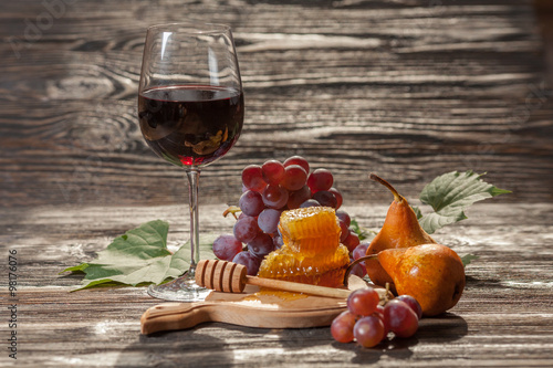 Glass of red wine, honeycomb, grapes on a wooden background. Selective focus.