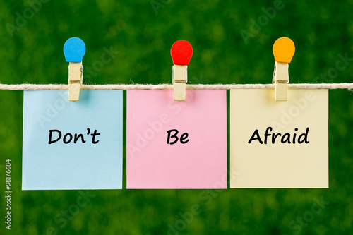 Words of Don't Be Afraid on sticky color papers hanging by a rope against blurred green background.