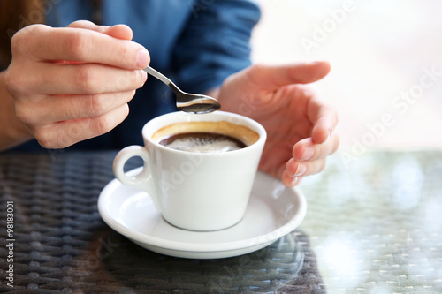 Cup of coffee with hands and spoon on table in cafe background
