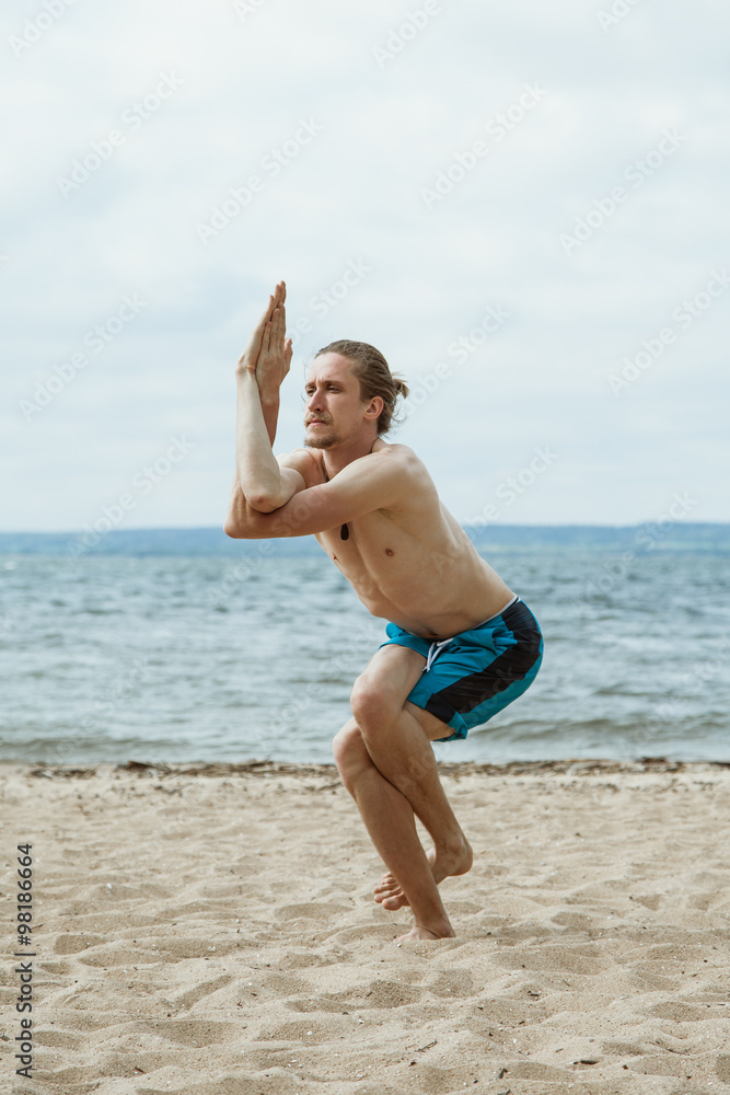 Fototapeta premium Man practices yoga on a sandy beach