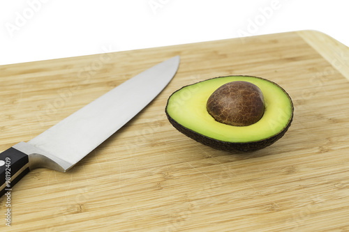 Knife and half cut avocado on a cutting board.