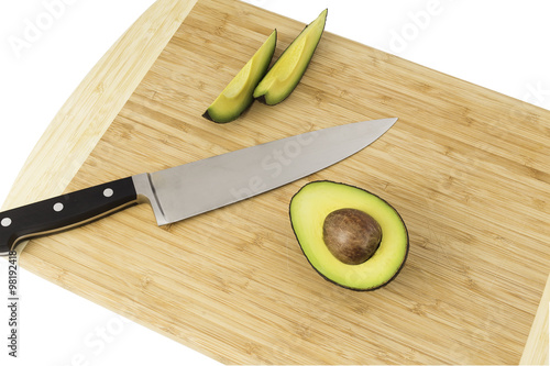 Knife with half cut and two slices of avocados on a cutting board.