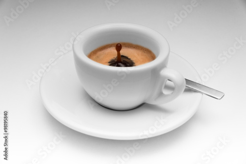 Espresso in einer schlichten weißen Tasse, auf dem Unterteller ein Löffel. Perfekter Tropfen aus dem Kaffee heraus. photo