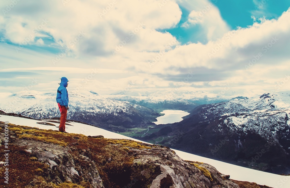 Obraz premium Vintage landscape of a tourist stands on a hilltop and look at the lake in the valley. Blue sky with clouds. Snowy mountains. Norway.