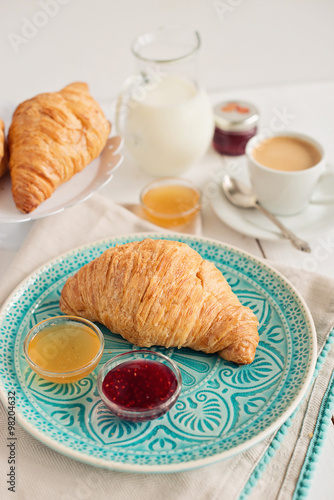 Romantic breakfast with croissant, coffee, milk, honey and jam on the table
