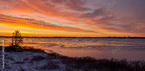sun sets over an icy muskeg pond in the subarctic of manitoba, canada. three windblown  trees in the midground photo