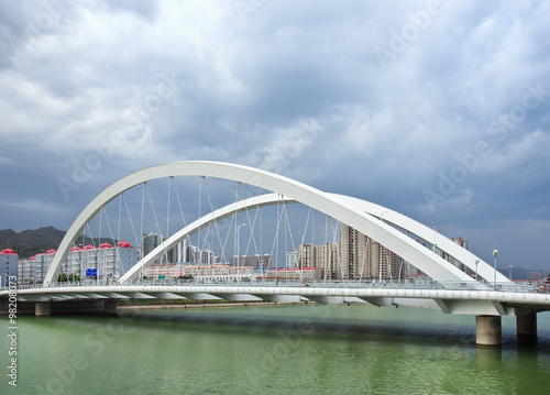 White bridge over a green canal with dramatic clouds, Zhangjiakou, China