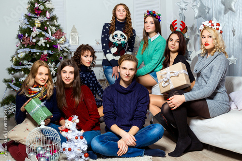 Company of boy and  seven girls sitting near the Christmas tree