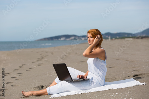 redheaded girl working at a laptop sitting on the beach © bigguns