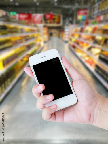 Female hand holding mobile smart phone on Supermarket blur backg