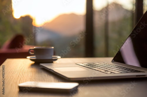 Computer Coffee Mug and Telephone on black wood table sun rising photo
