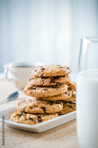 cookies stacked on each other on plate  glass of milk and cup of tea coffee  