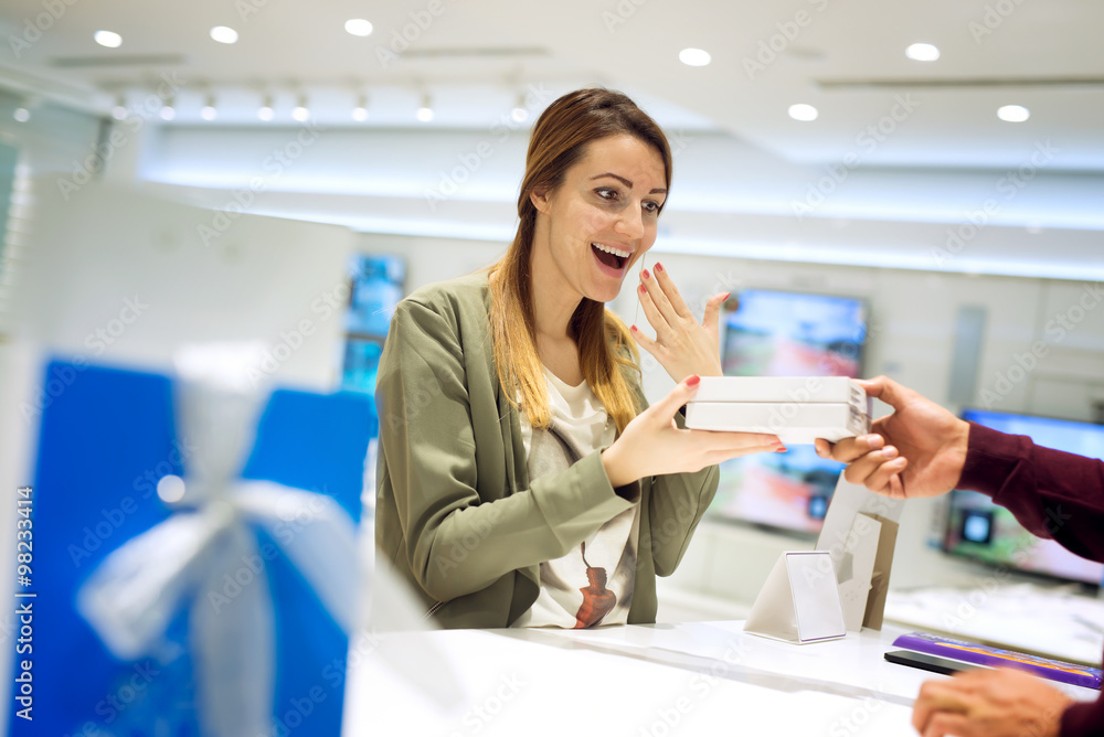 Beautiful female getting present at shop. She is taking present with one hand and laughing, covering her mouth with hand. Shallow depth of field. Beautiful female getting present at shop. She is taking present with one hand and laughing, covering her mouth with hand. Shallow depth of field.