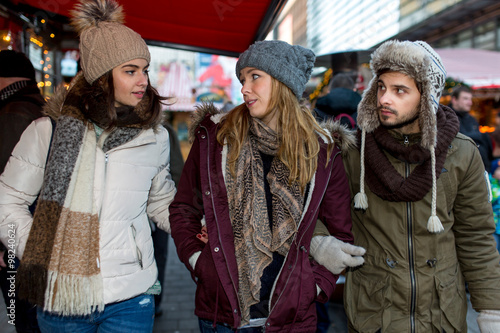Couple and Friend walk over the Christmas Market and talk to each other and watch the Stands