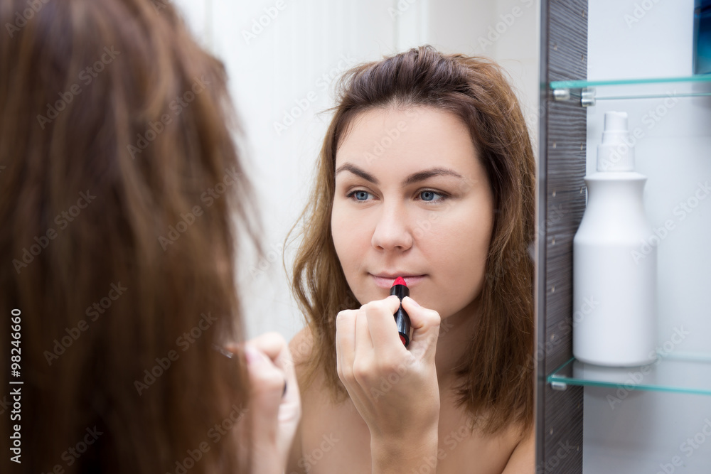 woman looking at mirror and applying lipstick in bathroom woman looking at mirror and applying lipstick in bathroom