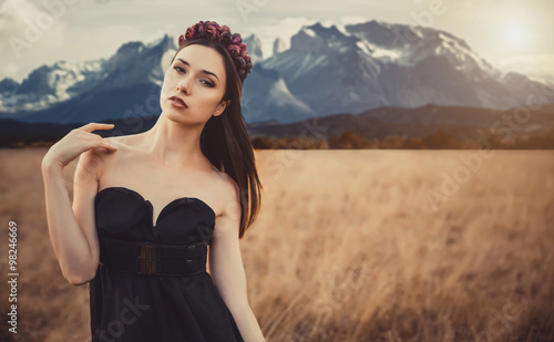 Beautiful girl in a black dress with flowers near mountains