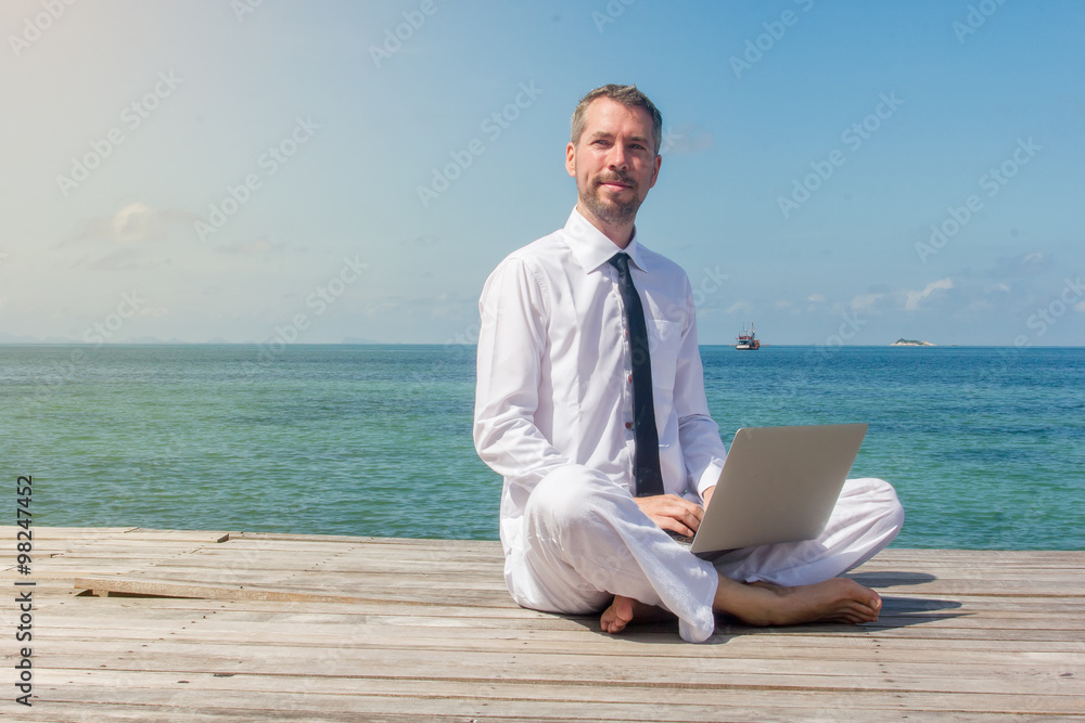 businessman doing yoga on a wooden bridge with a laptop