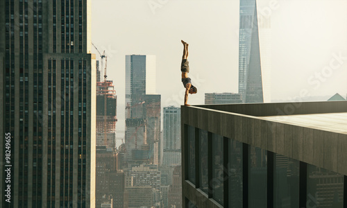 Fotografie, Obraz Man performs a handstand on the edge of a skyscraper