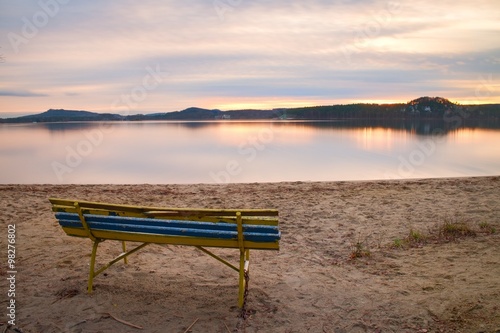 Colorful autumn evening. Empty wooden bench on beach of lake.