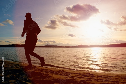 Silhouette of sport active man running on evening  beach water mountain and sunset cloudy sky background.