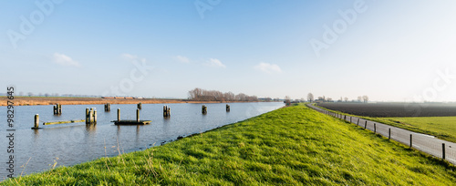 Grassy dike along a canal with wooden bollards photo