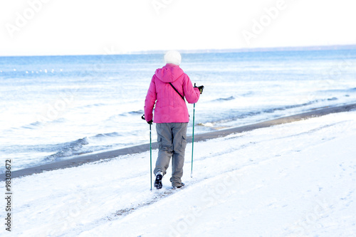 woman nordic walking along sea shore in winter