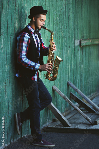 Canvas Print Young man playing on saxophone outside near the old wall