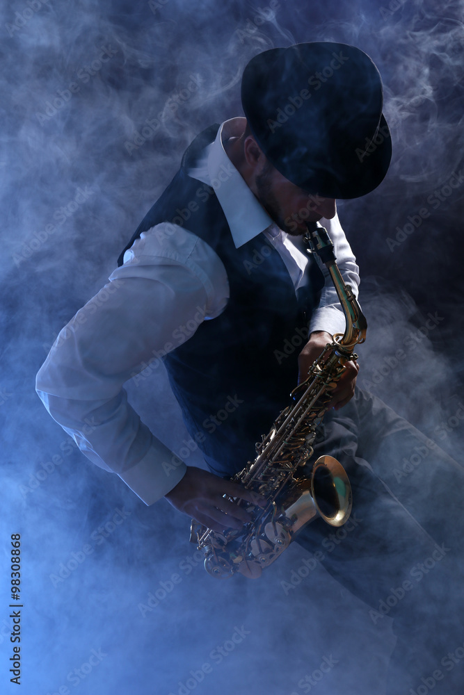 Naklejka premium Elegant saxophonist plays jazz on dark background in blue smoke