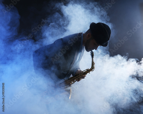Photography Elegant saxophonist plays jazz on dark background in a smoke