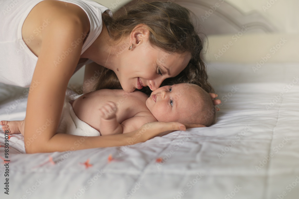 Mother and Newborn Baby Wake up in Morning in White bed in Light Room at Home Mother and Newborn Baby Wake up in Morning in White bed in Light Room at Home