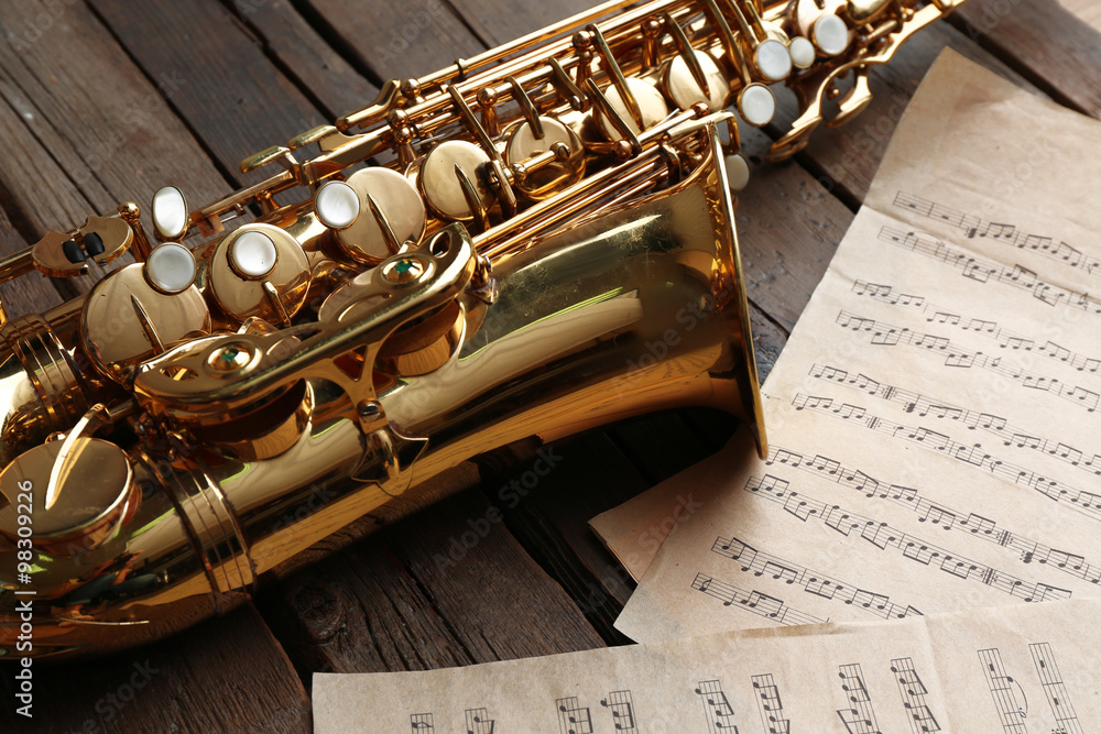 Naklejka premium Beautiful golden saxophone with musical notes on wooden background, close up
