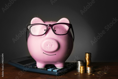 Piggy bank with glasses,coins and calculator on table , gray background