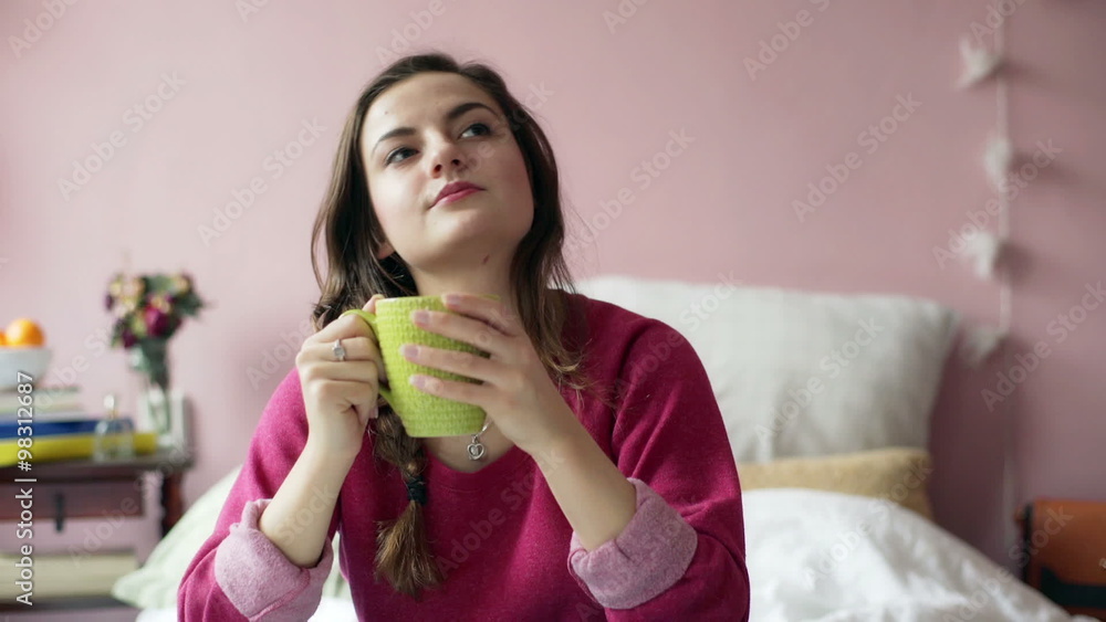 Teenage girl drinking tea and smiling to the camera in her bedroom
